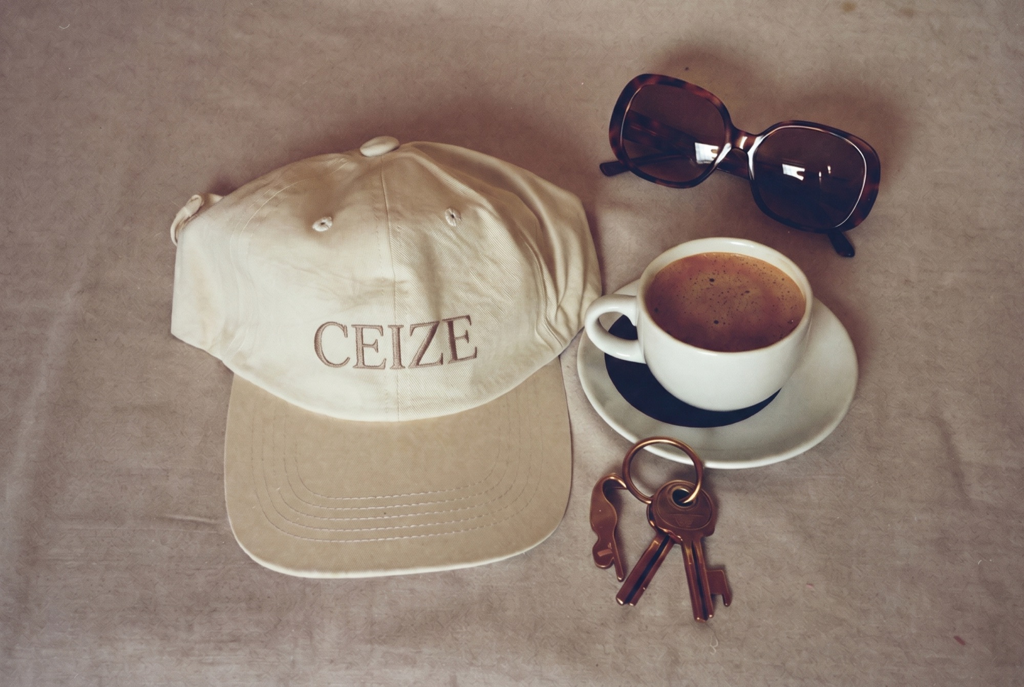 Flat lay of a plain cream cap, coffee, sunglasses and keys on linen